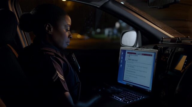 African american female police officer using a laptop in her patrol car at night