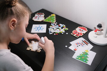 A girl makes a Christmas toy with her own hands from ceramic mosaic. Ceramic mosaic, DIY Christmas tree toy. Eco-friendly toy, educational activity for children.