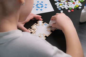 A girl makes a Christmas toy with her own hands from ceramic mosaic. Ceramic mosaic, DIY Christmas tree toy. Eco-friendly toy, educational activity for children.