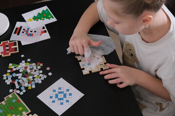 A girl makes a Christmas toy with her own hands from ceramic mosaic. Ceramic mosaic, DIY Christmas tree toy. Eco-friendly toy, educational activity for children.