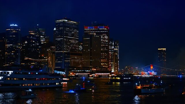Diverse boats stand on the dark waterscape watching night firework show. View on the beautiful high-rise building at the skyline of New York, USA.