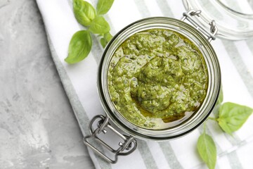 Fresh pesto sauce in jar with basil leaves on grey table, top view