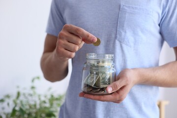 Man putting money into jar indoors, closeup