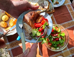 Family lunch. One person holds a plate with roasted chicken and vegetables in their hands.