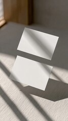 Two blank business cards resting on a textured surface with soft sunlight casting diagonal shadows, creating a minimalist and professional aesthetic.