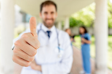 Close-up of a thumbs-up from a male doctor in a white coat and stethoscope gesturing approval,...