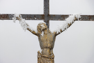 A winter crucifix with frost on a foggy background evokes themes of faith, suffering, and perseverance.