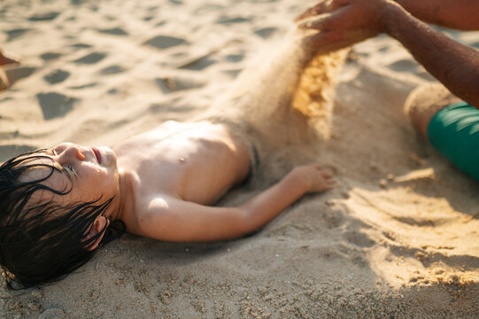 Child playing with sand on the beach with adult on a sunny summer day