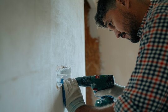 Manual worker using electric drill to install outlet during house renovation
