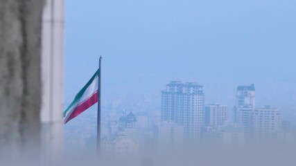 The Iranian flag waves against the backdrop of Tehran’s skyline, seen through layers of haze or fog. A poetic urban scene blending symbolism, atmosphere, and environmental mood.