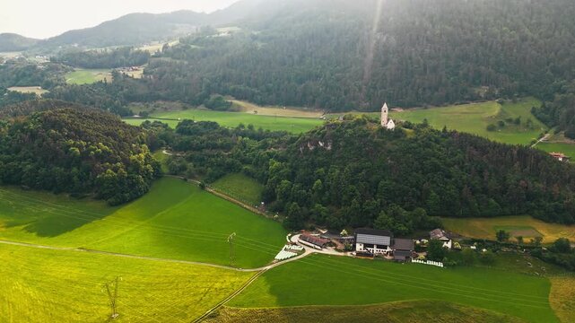 Chiesa di Santa Verena with meadows, pastures, and farm buildings in sunset light, aerial view. Dolomites countryside in South Tyrol, Northern Italy