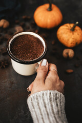 Female hand holding mug of hot chocolate, pumpkins and spices on rustic background, cozy autumn scene