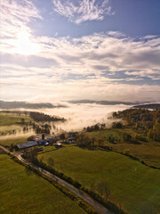 Drone aerial view of fog dissolving over a rural farm in the morning with massiv cloud formations. Vertical View optimized for mobile devices