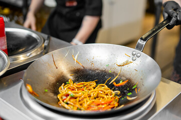 Professional kitchen scene with stir-fried noodles, vegetables, and glossy sauce in a wok. Chef in black gloves cooking Asian street food. Close-up, vibrant, dynamic composition.