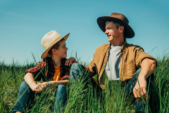 Father and son bonding outdoors wearing cowboy hats in summer grass