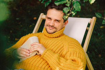Man relaxing outdoors under apple tree wearing yellow sweater in autumn