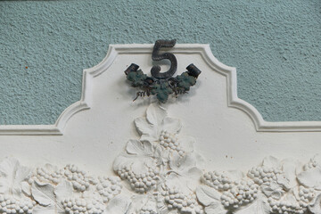 White grapevine relief with clusters on a gray-blue wall, complemented by a wrought iron number 5...