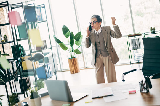 Professional senior businesswoman in a modern office discussing on phone passionately in an elegant outfit
