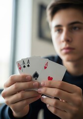 Teenager holding three aces playing card in his hand close to window
