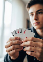 Young man holding four aces playing cards in his hands near the window