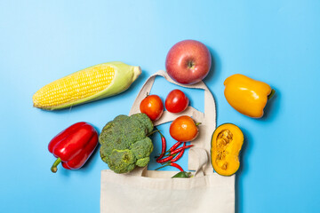 Flat lay of fresh vegetables and fruits with reusable cotton tote bag on blue background. Perfect for eco friendly shopping, organic food, vegan lifestyle, healthy diet, and sustainability concepts.