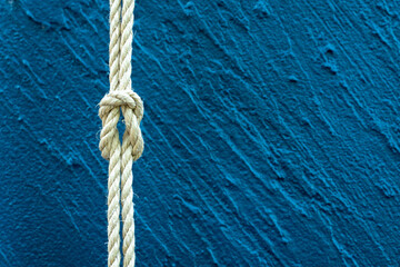 Close-up of strong rope tied in a knot against textured blue wall background. Symbol of strength, security, connection, teamwork, stability, and resilience for business, maritime, and life concepts.