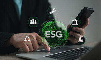 Business professional using digital ESG icons on laptop and smartphone, symbolizing sustainability, environmental responsibility, social impact, governance, and eco-friendly corporate strategy.