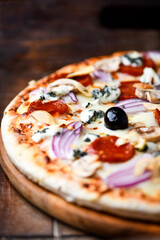 Pizza with chorizo ​​sausage, mozzarella cheese, and black olives. Rustic wooden background. Soft focus.	