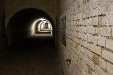 Old brick tunnel with dim lighting. Dark underground corridor with arched ceiling, concept of history, abandoned places or suspense