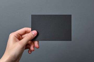 A hand holds a blank black card against a gray backdrop