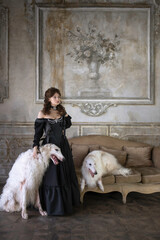 An elegant dark-haired girl with two greyhounds in a vintage interior