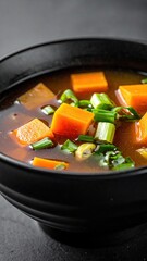 Hearty Vegetable Soup with Carrots and Green Onions in Black Bowl.