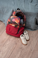 white pair of children's sneakers and a red checkered colorful backpack lie on the floor in the room. Cleaning and discipline. Decluttering