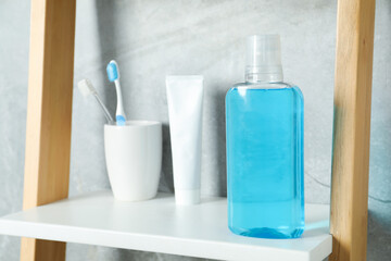 Bottle of mouthwash, toothbrushes and toothpaste on shelf in bathroom, selective focus