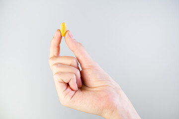 Female hand holding yellow pill isolated on gray background.