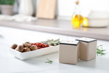 Salt, pepper shakers and spices on white marble table in kitchen, closeup