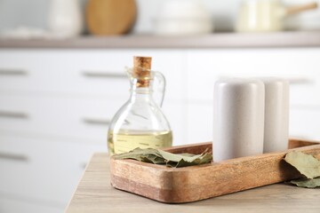 Salt and pepper shakers, dry bay leaves and bottle of oil on wooden table indoors, closeup. Space for text