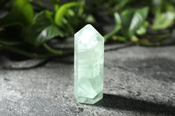 Beautiful fluorite gemstone and green leaves on grey table, closeup
