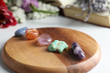 Different beautiful gemstones, book and flowers on white table, closeup