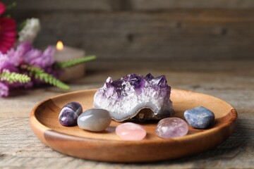 Different beautiful gemstones, flowers and burning candle on wooden table, closeup