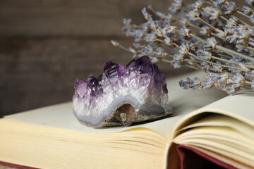 Beautiful amethyst gemstone, book and lavender flowers on blurred background, closeup
