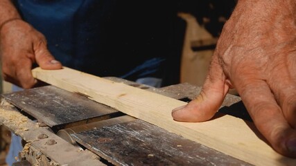 A man's hand runs a wooden plank through a woodworking machine that grinds and smooths the surface. Home woodworking workshop, wood processing.