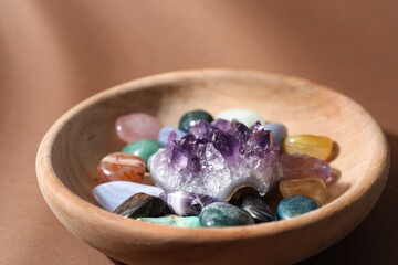 Different beautiful gemstones in bowl on brown background, closeup