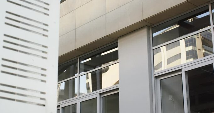 White perforated panel appearing on left and sliding across facade covering windows under sunny sky