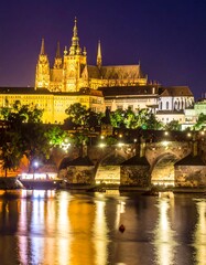 Fototapeta premium Night view of a grand castle complex illuminated, overlooking a stone bridge and calm river reflecting city lights