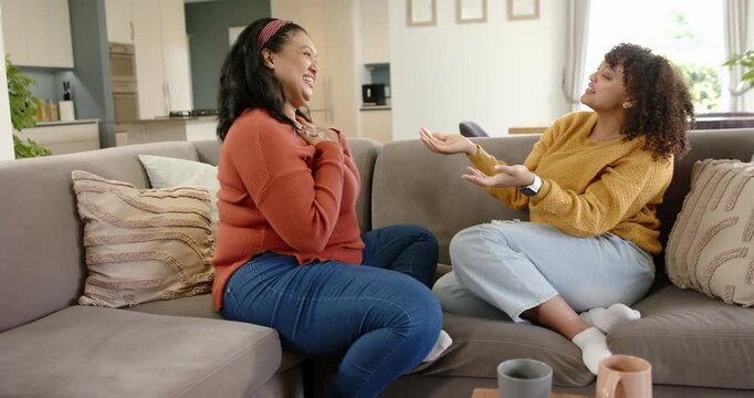 Female friends playing hand-clapping game, reacting to palm gesture, and hugging on sofa at home