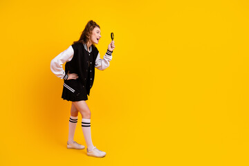 Fototapeta premium Cheerful young student with magnifying glass in trendy jacket posing on bright yellow background, exploring and smiling