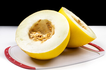 A yellow honeydew melon cut in half on a red cutting board isolated on white