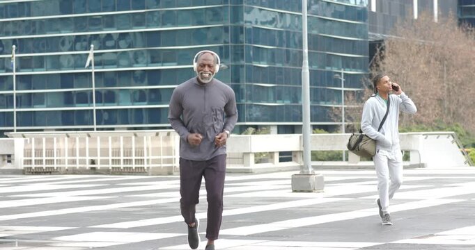 Jogging on crosswalk Senior African American man pausing massaging knee and stretching hamstring