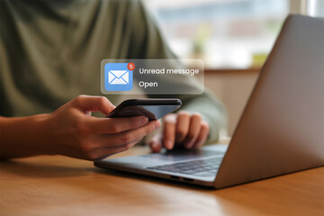 Person Checking Smartphone for New Email Notification with Unread Messages While Working on Laptop in Modern Workspace
